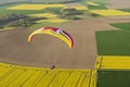 Colorful Paramotor seen from the sky over the fields of yellow rapeseed in spring