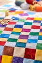 Colorful part of quilt sewn from square pieces, spools of thread, quilting and sewing accessories