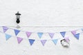 Colorful Party flags bunting hanging on white wall background with wall lamp light. Minimal hipster style design.