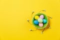 Colorful pastel painted Easter eggs in basket with green grass, white flowers lilies of the valley isolated on yellow Royalty Free Stock Photo