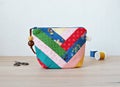 Colorful patchwork notions bag, retro scissors and thread spools on wooden desk Royalty Free Stock Photo