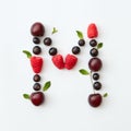 Colorful pattern of letter M english alphabet from natural ripe berries - black currant, cherries, raspberry, mint leaf Royalty Free Stock Photo