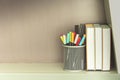 Colorful pen in metal pen pot and books on shelve