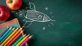 Colorful pencils and apples beside a chalkboard rocket drawing. Creative education concept in a classroom setting Royalty Free Stock Photo