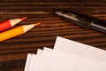 Colorful pencils, ballpoint pens, and white sheets of paper on a wooden table Royalty Free Stock Photo