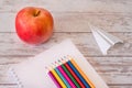 Colorful pencils on the open note pad and red apple with paper airplane on a wooden desk. Concept of begining of the school year Royalty Free Stock Photo