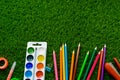 Colorful pencils, paints, school supplies and plasticine on green grass top view. Stationery. Back to school concept