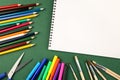 Colorful pencils, scissor, felt tip markers, paint brushes and blank sketchbook sheet with copy space on dark green background. Ba Royalty Free Stock Photo