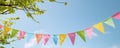 Colorful Pennant String Decoration In Green Tree Against Blue Sky