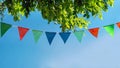 colorful pennant string decoration in green tree foliage on blue sky, summer party background Royalty Free Stock Photo