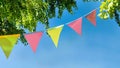 colorful pennant string decoration in green tree foliage on blue sky, summer party background Royalty Free Stock Photo