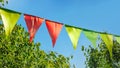 colorful pennant string decoration in green tree foliage on blue sky, summer party background Royalty Free Stock Photo