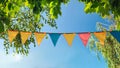 colorful pennant string decoration in green tree foliage on blue sky, summer party background Royalty Free Stock Photo