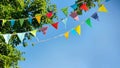 colorful pennant string decoration in green tree foliage on blue sky, summer party background Royalty Free Stock Photo