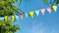 colorful pennant string decoration in green tree foliage on blue sky, summer party background Royalty Free Stock Photo