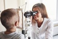 Colorful picture. Little boy having test for his eyes with special optical apparatus by female doctor