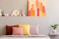 Colorful pillows on bed in grey bedroom interior with poster and clock on bedhead. Real photo