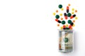 Colorful pills spilled from a bottle made of money, on white background. The Concept of Drug Purchase. Royalty Free Stock Photo