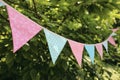 Colorful pink and blue triangular bunting flags hanging among trees. Summer garden party. Outdoor birthday or wedding Royalty Free Stock Photo