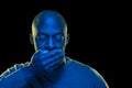 Black man with mouth covered by hand and eyes closed. Blue light