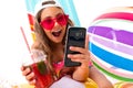 Colorful portrait of a girl with summer glasses, a cocktail and a phone on the background of inflatable swimming