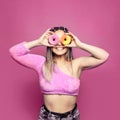 Colorful portrait of a satisfied pretty woman with donuts having fun on pink background