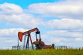 Colorful pump jack on oil well - low horizon on prairie with green grass and wild flowers - big blue cloudy sky - room for text Royalty Free Stock Photo