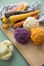 Colorful rainbow cauliflower and carrots veggies in purple, white, orange and yellow with wooden board and kitchen towel on pastel Royalty Free Stock Photo