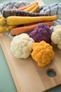 Colorful rainbow cauliflower and carrots veggies in purple, white, orange and yellow with wooden board and kitchen towel on pastel