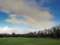 Colorful rainbow in a cloudy sky over trees in a forest and a green field. Nature background Royalty Free Stock Photo