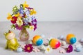 Colorful rainbow Easter eggs and funy frog with spring flowers on gray stone background