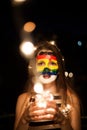 Colorful rainbow face art on a young girl at night with lights in a hands and bokeh