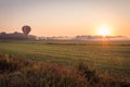 Colorful rainbow hot air balloon lifts off over a farm field at sunrise Royalty Free Stock Photo