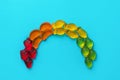 Colorful rainbow made from multicolored fruits gummy jelly candies strawberries oranges pineapples limes on blue sky background