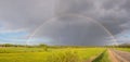 Colorful rainbow after the storm passing over a field near the road Royalty Free Stock Photo