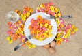 Colorful ravioli pasta with a white plate, two forks, three eggs and a glass of water on canvas