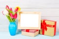 Colorful red spring tulip flowers in nice blue vase and blank photo frame with giftboxes on light wooden background as greeting ca Royalty Free Stock Photo