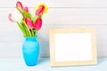 Colorful red spring tulip flowers in nice blue vase and blank photo frame on light wooden background as greeting card. Mothersday Royalty Free Stock Photo