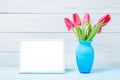 Colorful red spring tulip flowers in nice blue vase and blank photo frame on light wooden background as greeting card. Mothersday Royalty Free Stock Photo