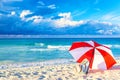 Colorful red and white umbrella with beach bag on the ocean beach against beautiful blue sky and clouds. Relaxation, vacation Royalty Free Stock Photo