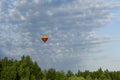 Colorful red and yellow hot air balloon flying over the green forest against a deep blue sky and clouds. Royalty Free Stock Photo