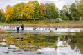 Colorful reflections of autumn trees at Venta waterfall and a couple watching it, Kuldiga, Latvia