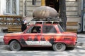 Colorful retro Soviet red car with artistically pictures and a jug on the roof to fun and attract attention at the entrance to the