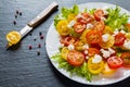 Colorful salad, fresh green leaves and sliced red and yellow cherry tomatoes, white plate, knife, black stone background Royalty Free Stock Photo