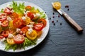 Colorful salad, fresh green leaves and sliced red and yellow cherry tomatoes, white plate, knife, black stone background Royalty Free Stock Photo