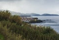 Colorful small coastal village houses on rocky lava shore above Atlantic ocean with sea water waves, cloouds and moody Royalty Free Stock Photo