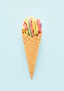 Colorful sour jelly candies in sugar sprinkles in an ice cream cone on a blue background. Flat lay, vertical.