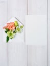 Colorful spring flowers in envelope and white sheet on wooden background.