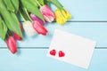 Colorful spring tulip flowers with blank photoframe and hearts on light blue wooden background as greeting card with free space. M Royalty Free Stock Photo