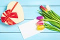Colorful spring tulip flowers with decorative giftbox and blank photo on light blue wooden background as greeting card. Mothersday